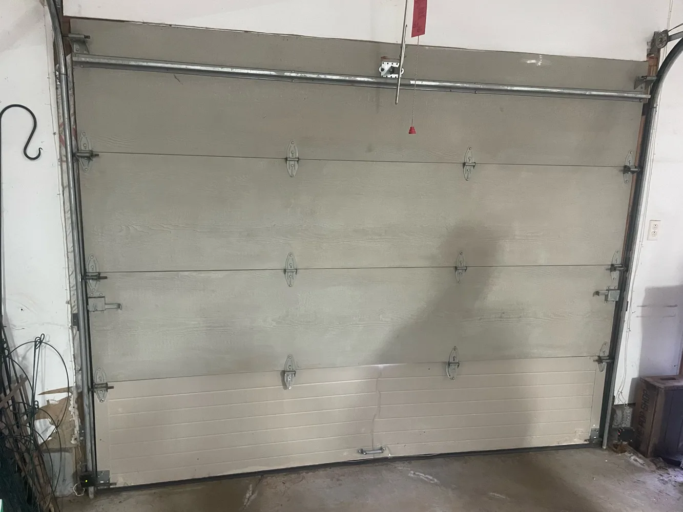 A tall sectional garage door seen closed from inside a garage, its bottom section noticeably newer and lighter than the three weathered sections above it, with hinges and vertical track on both sides.